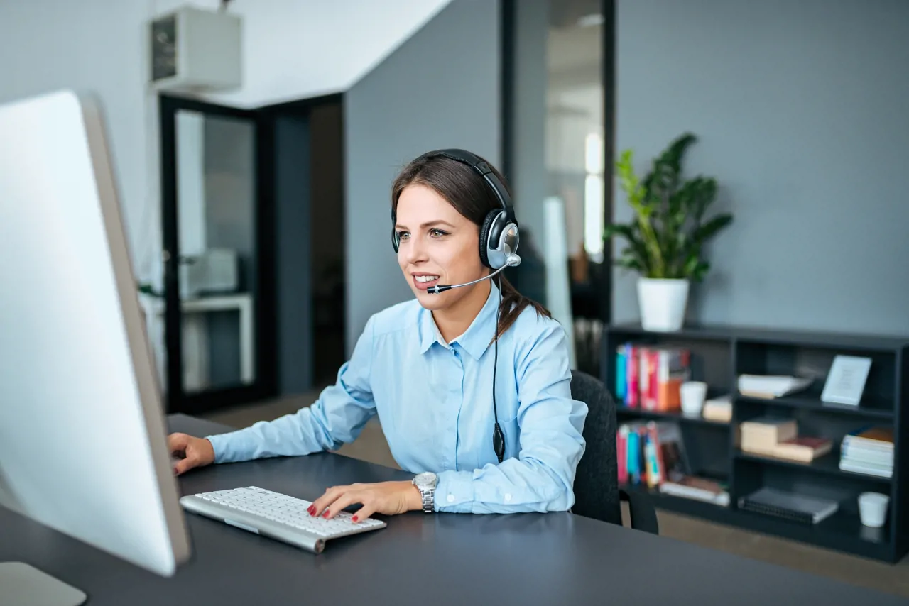 A woman working in customer service with a headset on on a laptop
