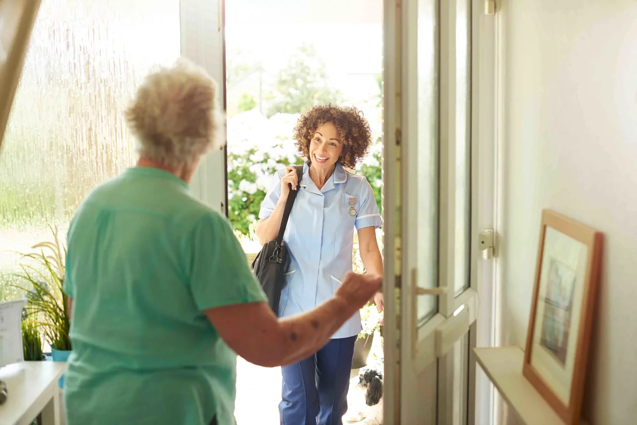 A healthcare assistant being welcomed into an elderly patient's home