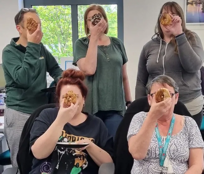 Meridian's back office team hiding their faces with donuts