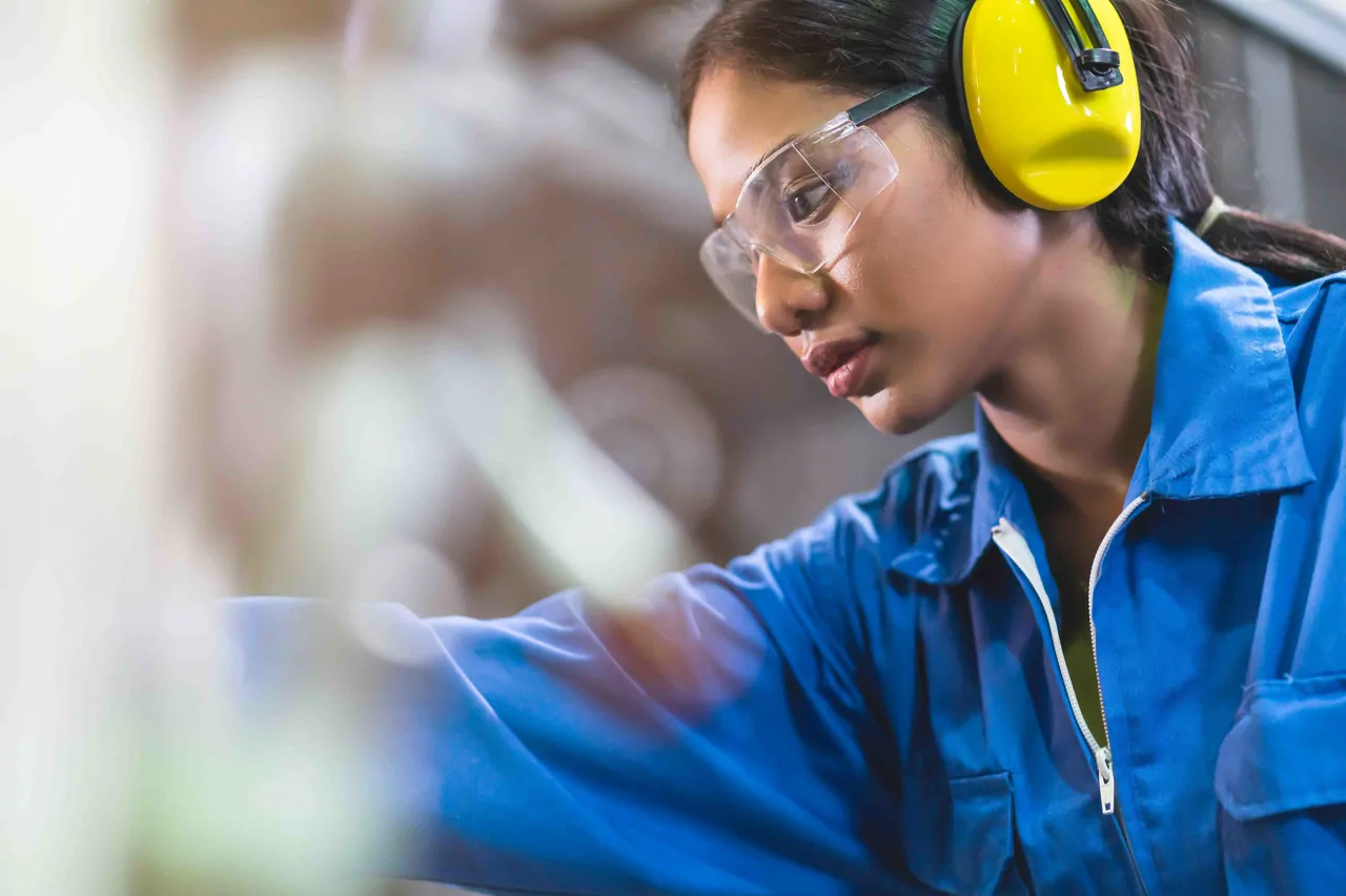 A female factory worker wearing ear defenders and safety goggles
