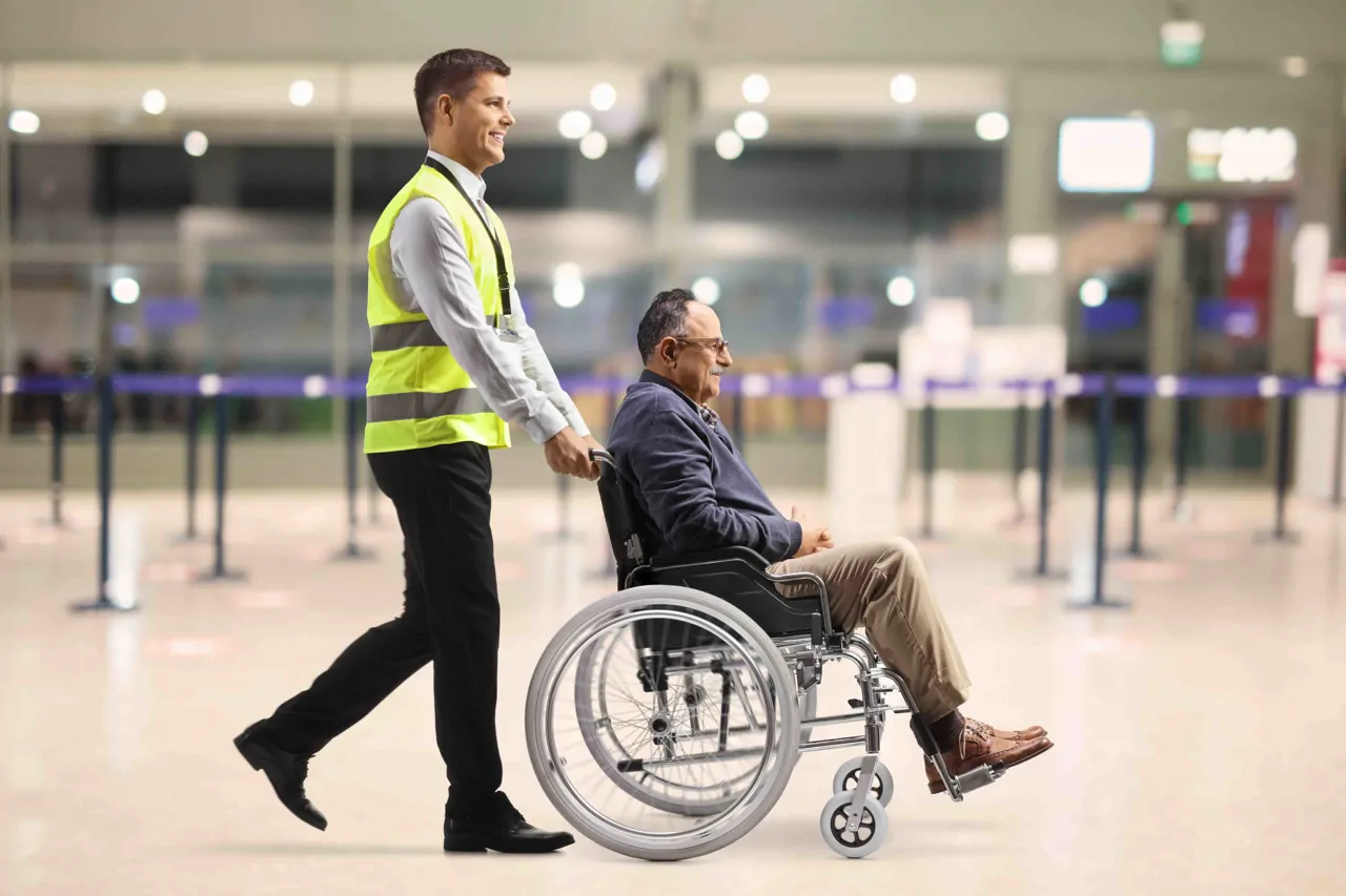 Airport worker assisting a gentleman in a wheelchair navigate the airport