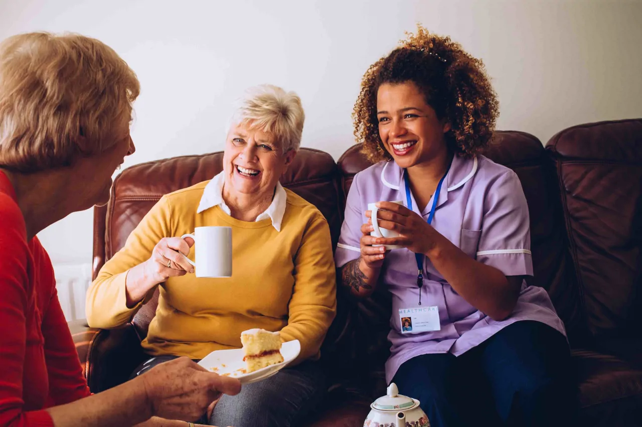 Female care worker with two patients smiling with a cup of tea and cake