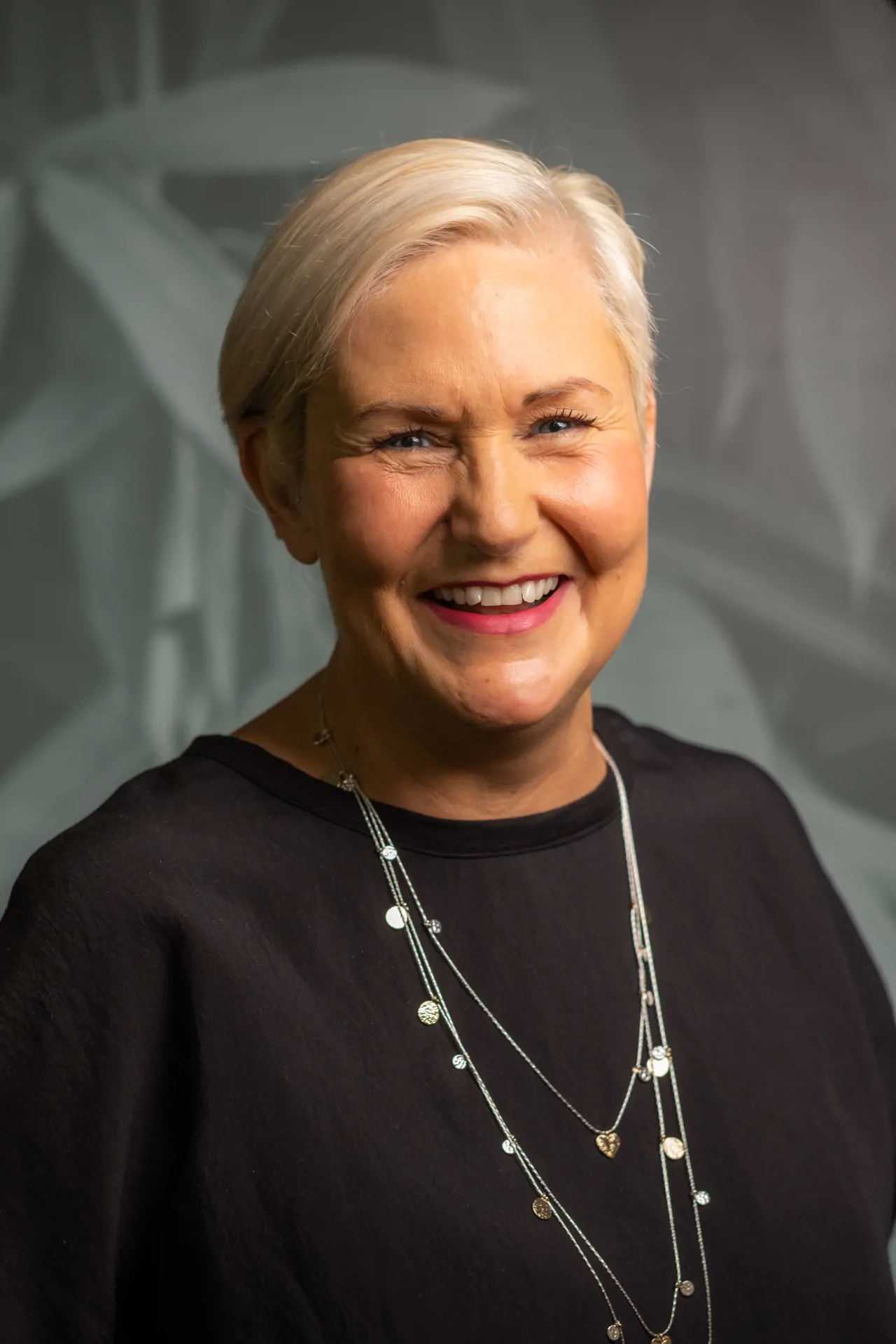 Woman with short platinum hair and wearing a necklace smiling for headshot photo